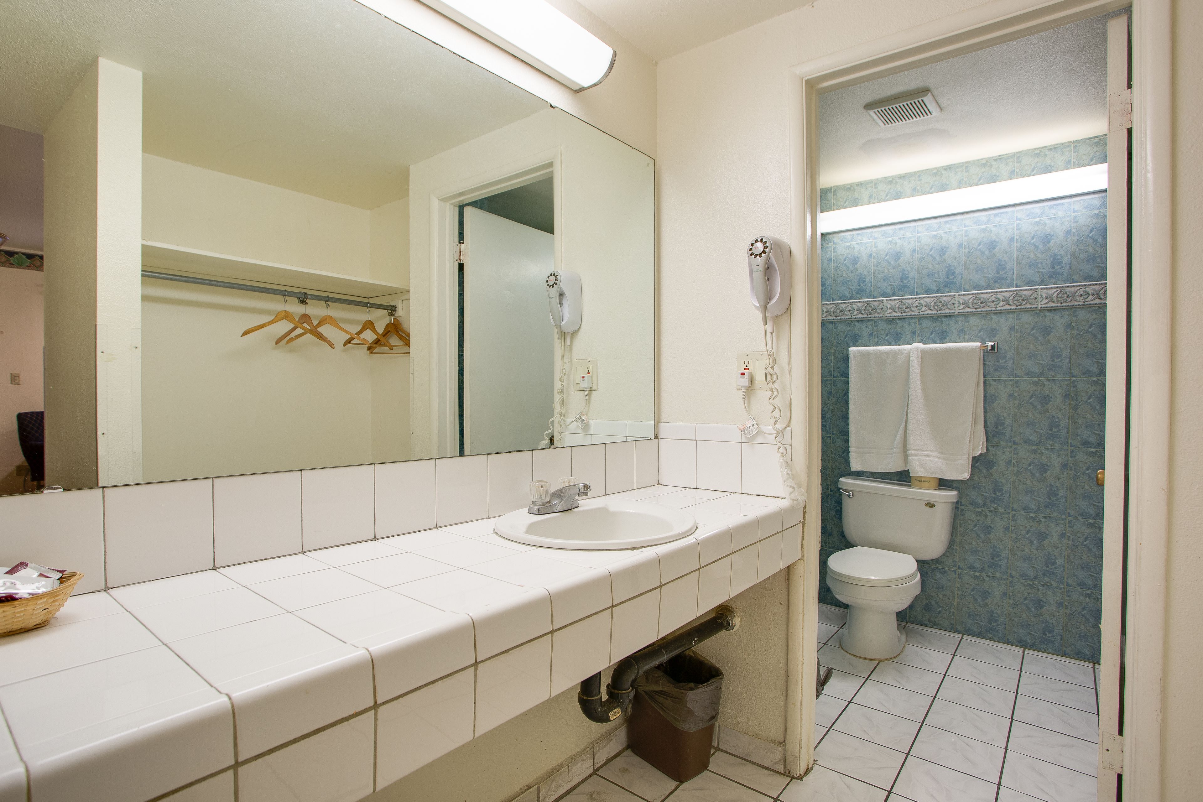 A bathroom with a white sink, a mirror, a white toilet, and a blue-tiled shower area.