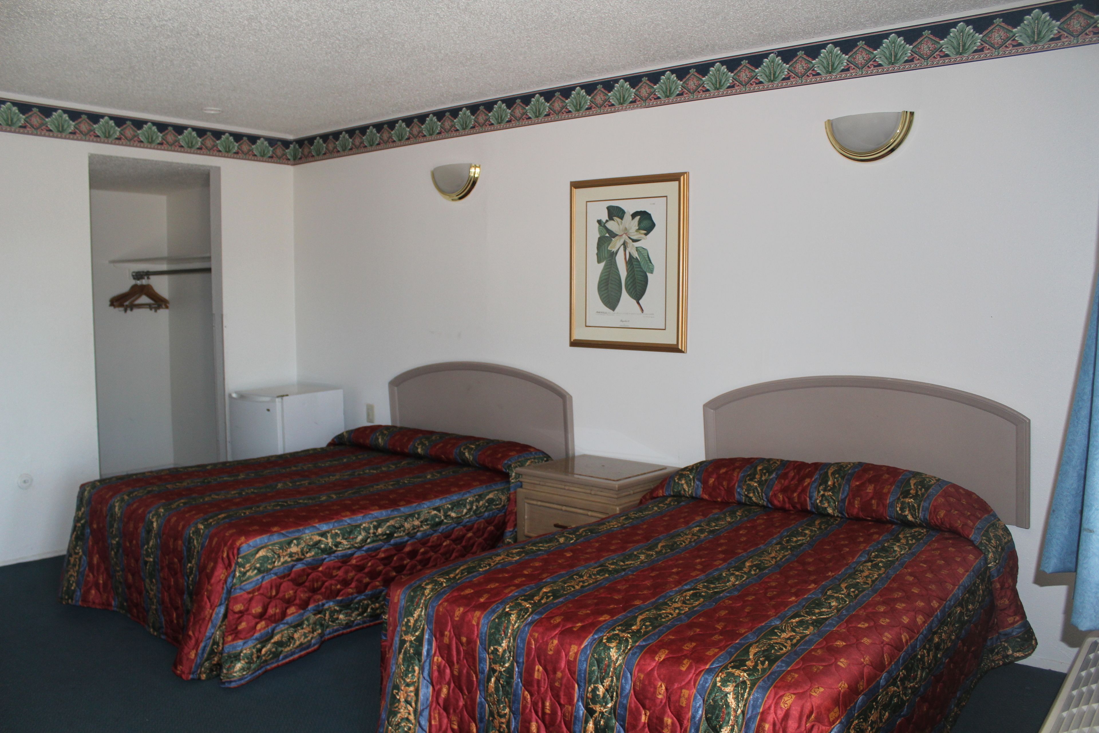 A room with two beds, a framed botanical print on the wall, and a door leading to a bathroom.