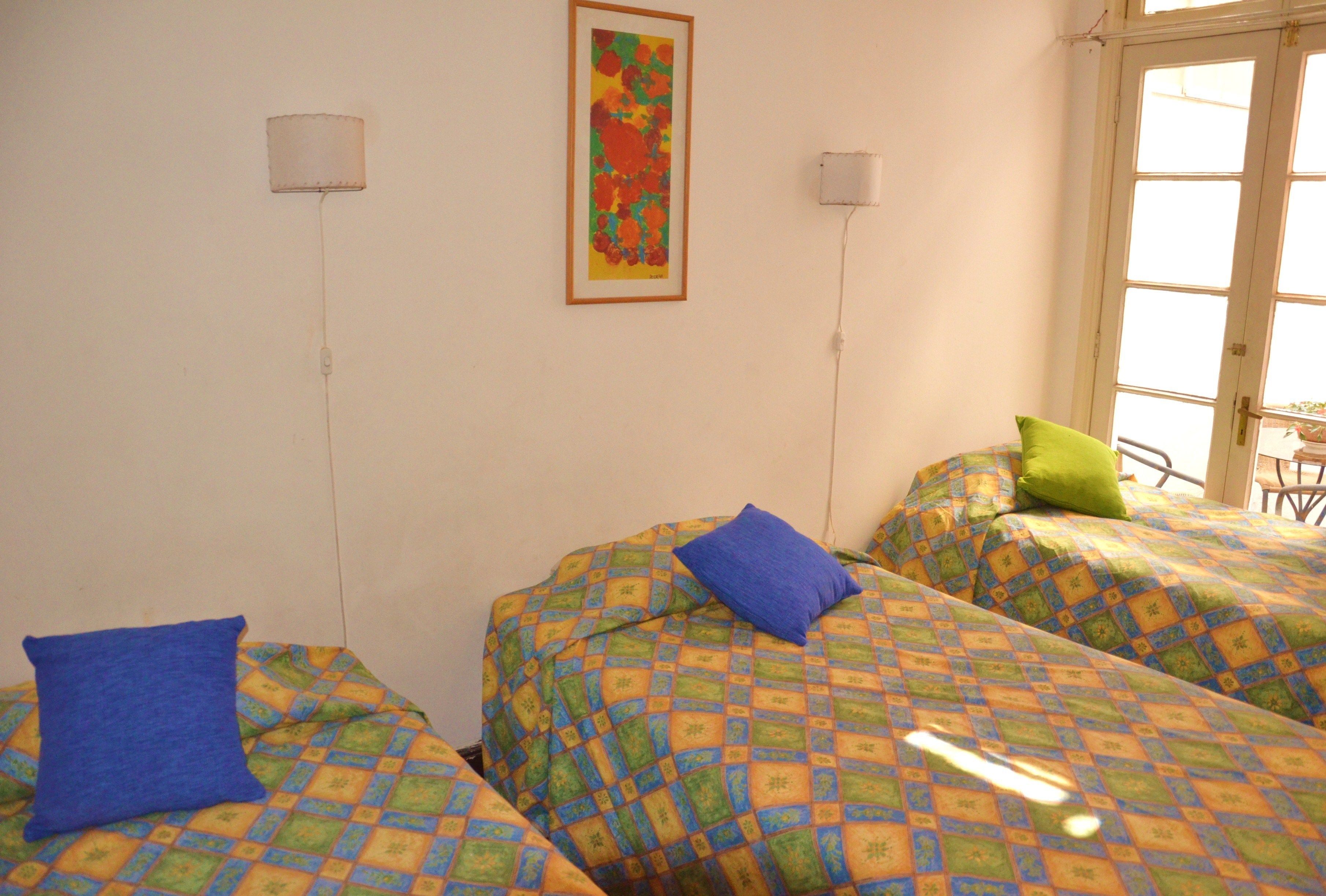 A room with two beds, each with a patterned bedspread and pillows. There is a framed artwork on the wall and a window with a view.
