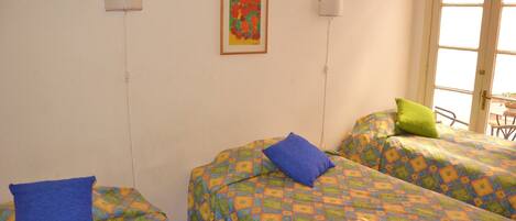 A room with two beds, each with a patterned bedspread and pillows. There is a framed artwork on the wall and a window with a view.