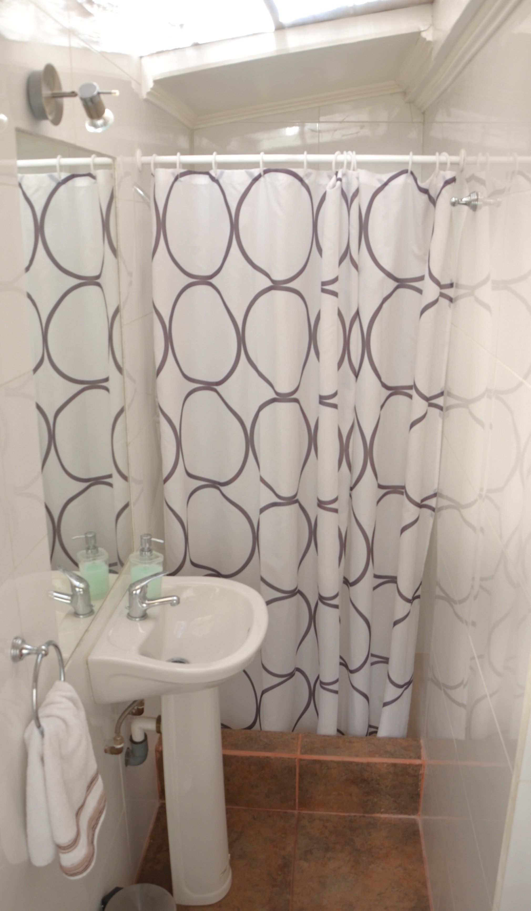 A bathroom with a white sink, two faucets, and a mirror above it. There is a shower curtain with a circular pattern.