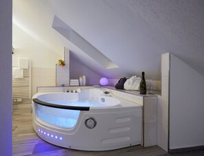 Un baño moderno con un jacuzzi integrado, un perchero, una botella de champán y una copa de vino sobre el mostrador.