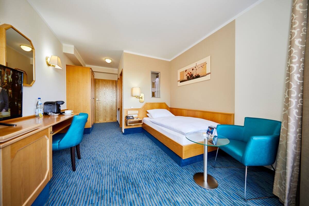 Une chambre d’hôtel comprenant un lit, un bureau avec une chaise, une petite table avec un plateau en verre, une table de chevet et un miroir.