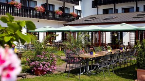 An outdoor dining area with tables and chairs, surrounded by potted plants and flowers. - Hotel Sonnenhof Dietzenbach (Dietzenbach)