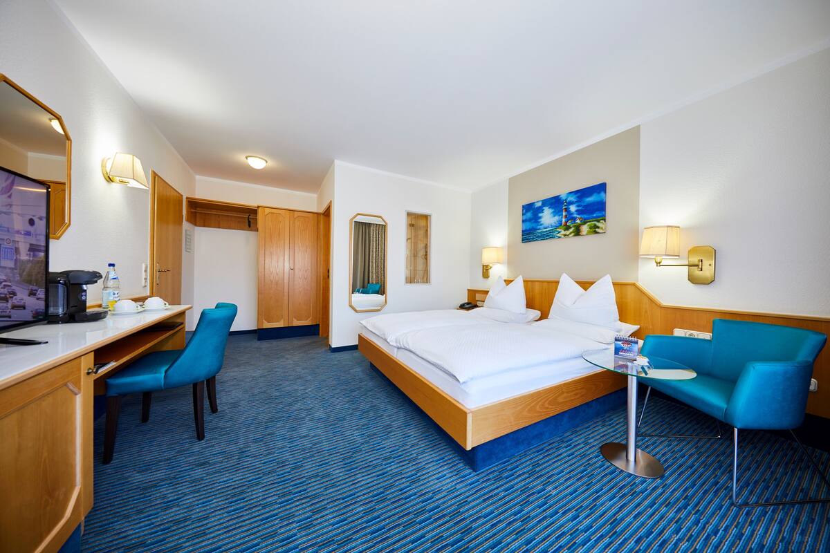 Une chambre d’hôtel comprenant un lit, un bureau avec une chaise, un canapé, une petite table et un tableau au mur.