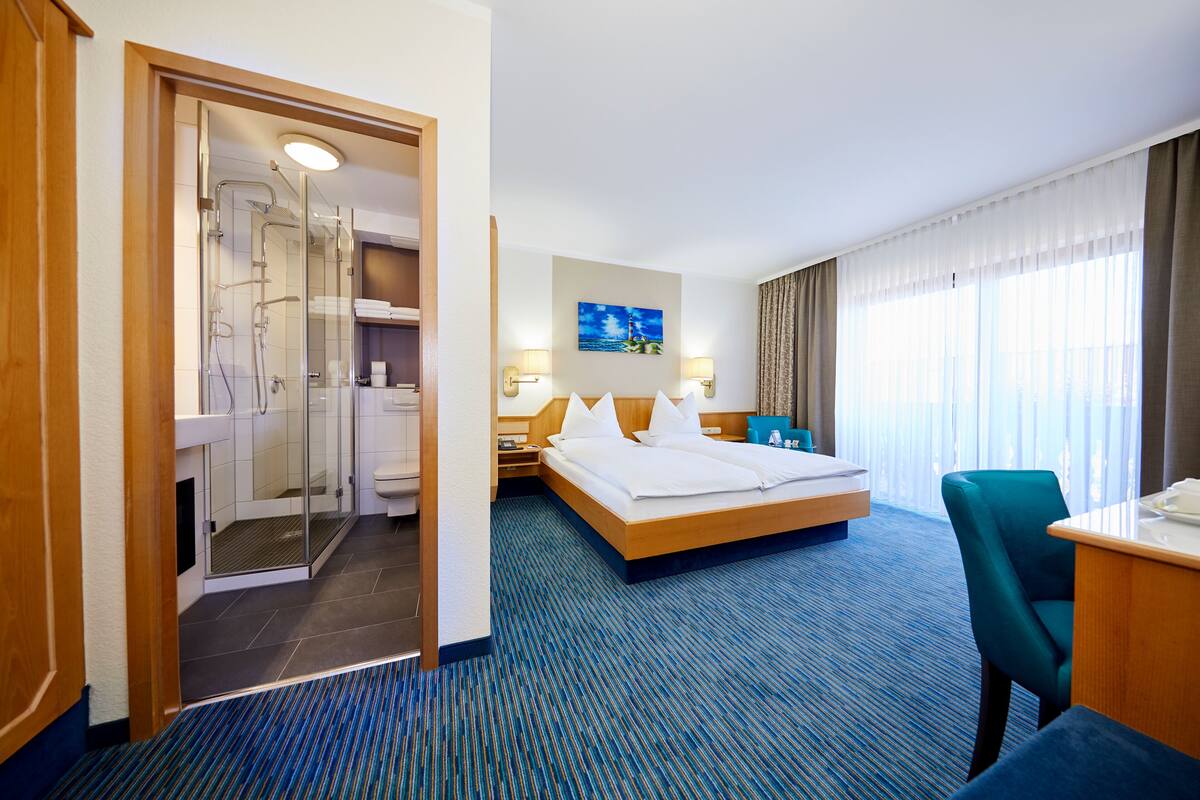 Une chambre d’hôtel avec un grand lit, un bureau, une chaise, un espace douche et un tableau au mur.