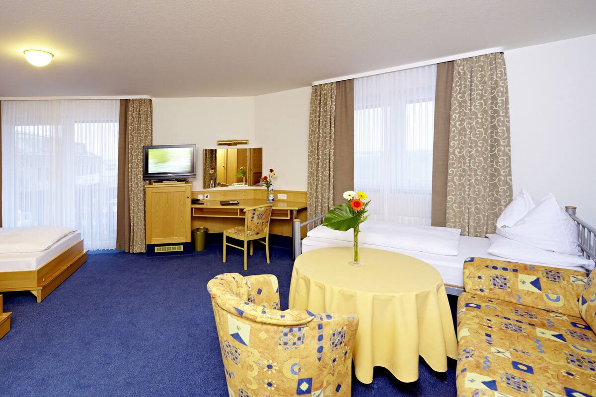 Une chambre d’hôtel avec deux lits simples, un bureau avec une chaise, une télévision et une petite table ronde agrémentée d’un vase de fleurs.