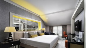A modern hotel room with a large bed, two bedside tables, a TV, and a seating area with a chair and a small table. - Mercure Istanbul Bomonti (Istanbul)