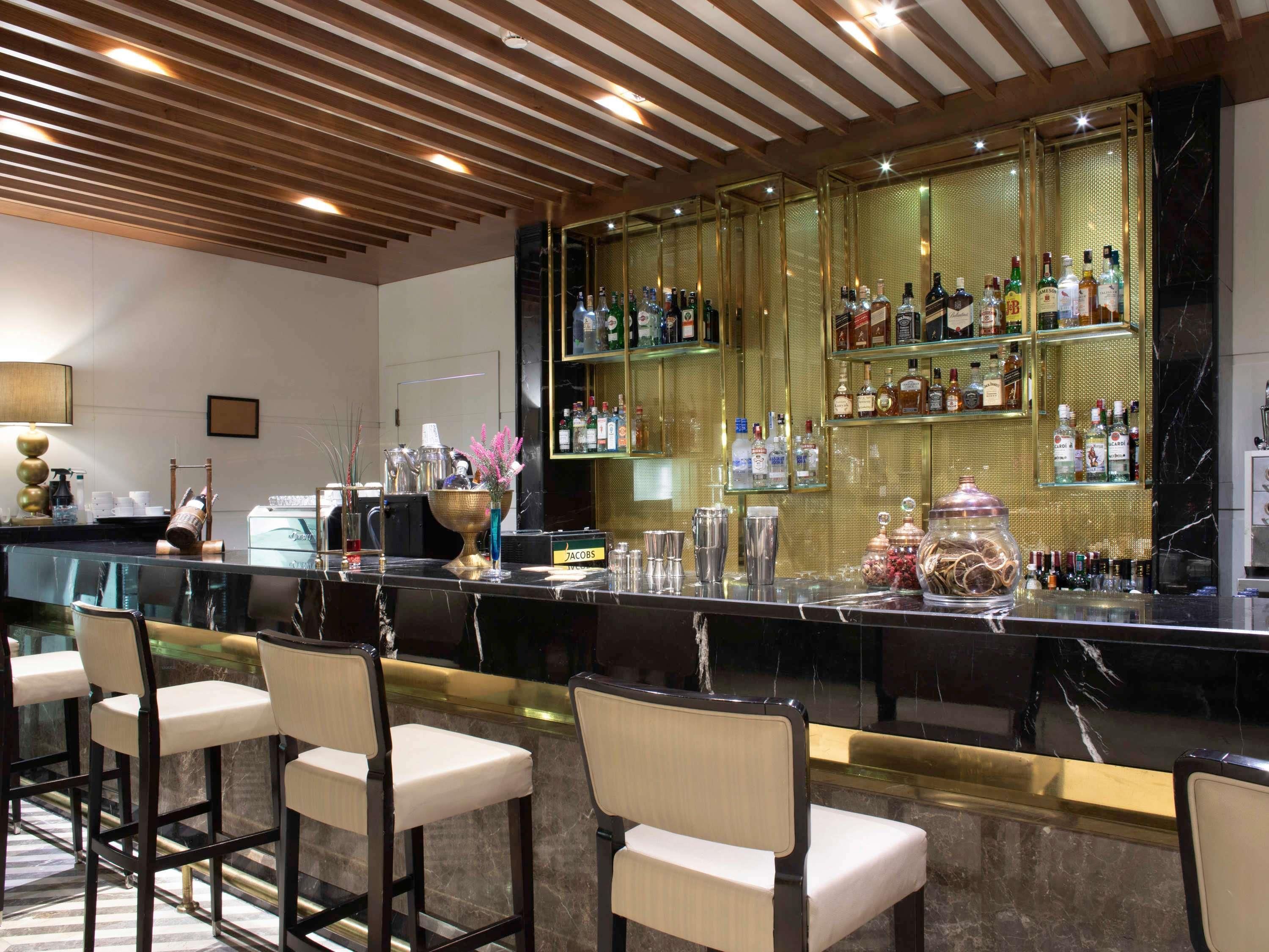 A bar area with a marble countertop, bar stools, and a variety of liquor bottles.