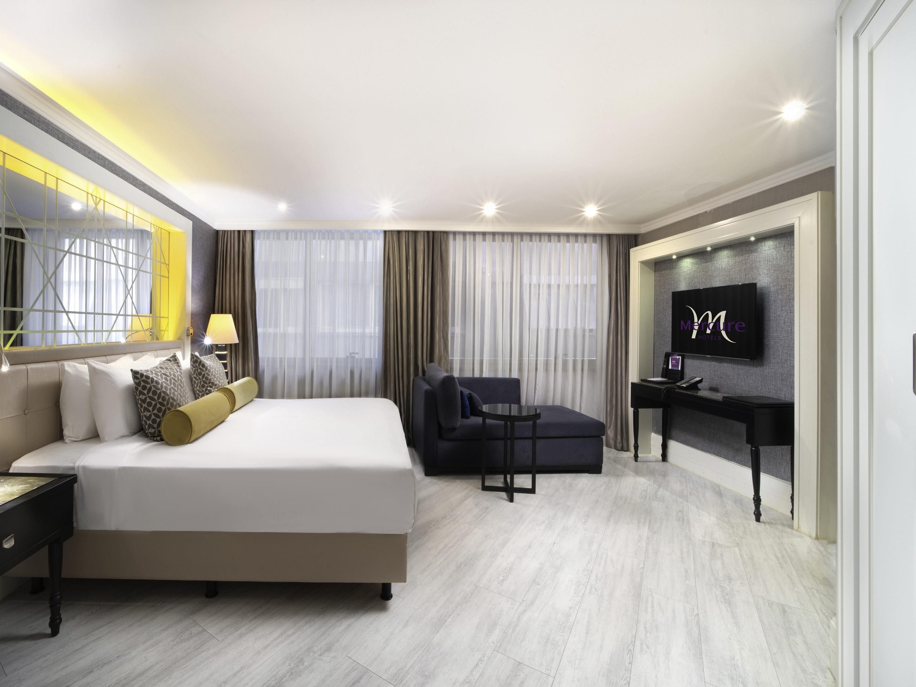 A modern hotel room with a large bed, a desk, a chair, and a TV.