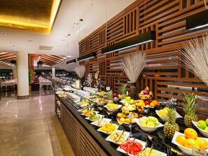 Buffet com variedade de frutas e legumes, painéis de madeira nas paredes e design moderno no teto.
