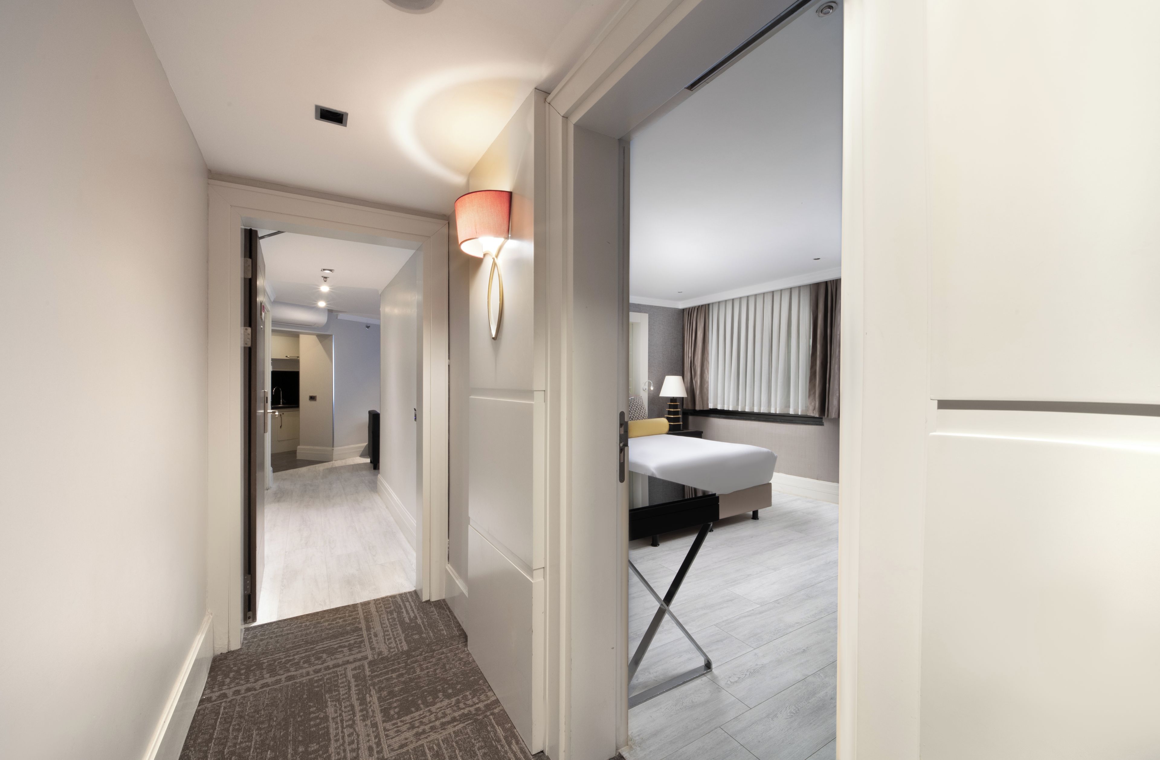 A hotel room with a bed, bedside table, lamp, and a view of the hallway.
