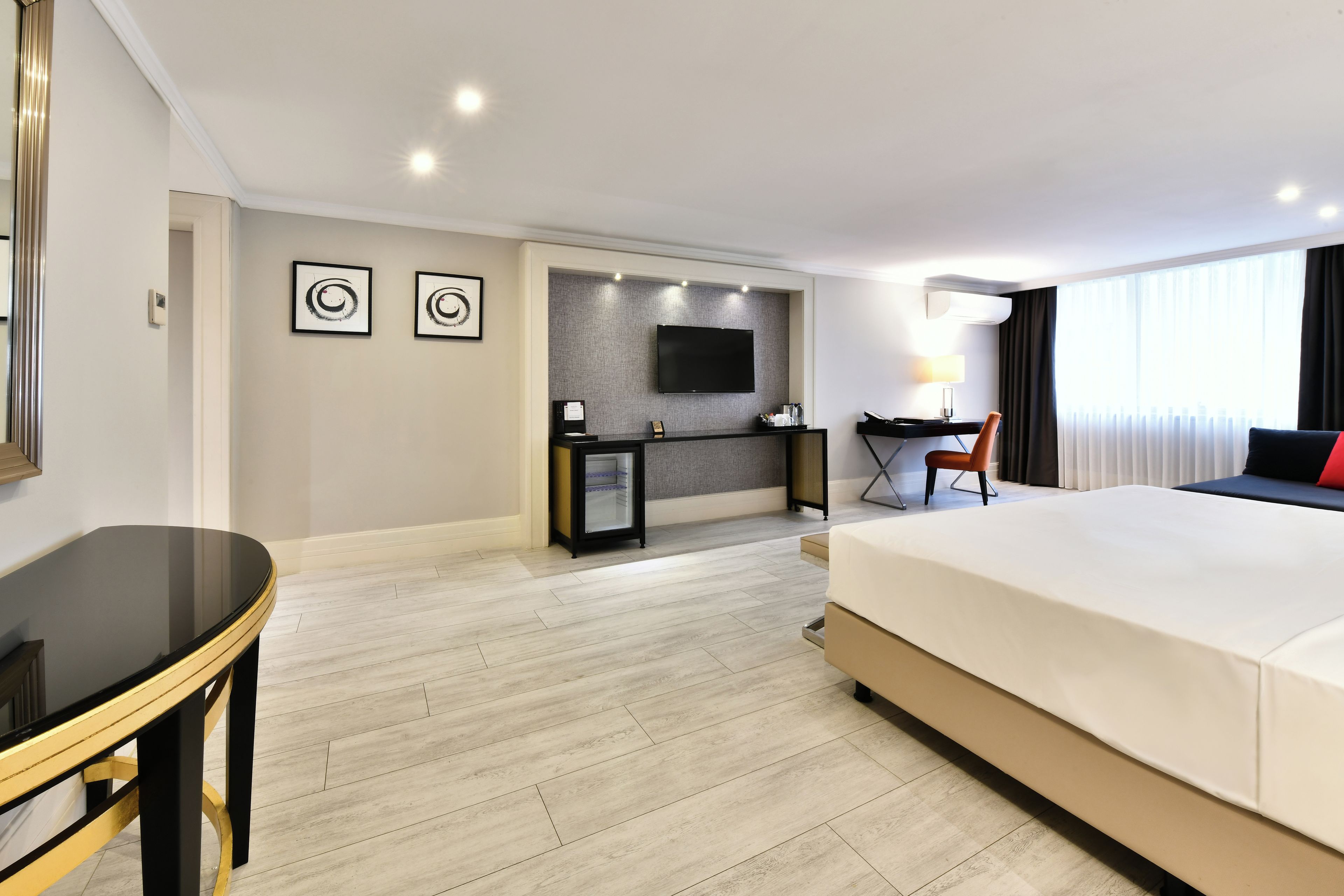 A hotel room with a large bed, a desk, a chair, a TV, and artwork on the wall.