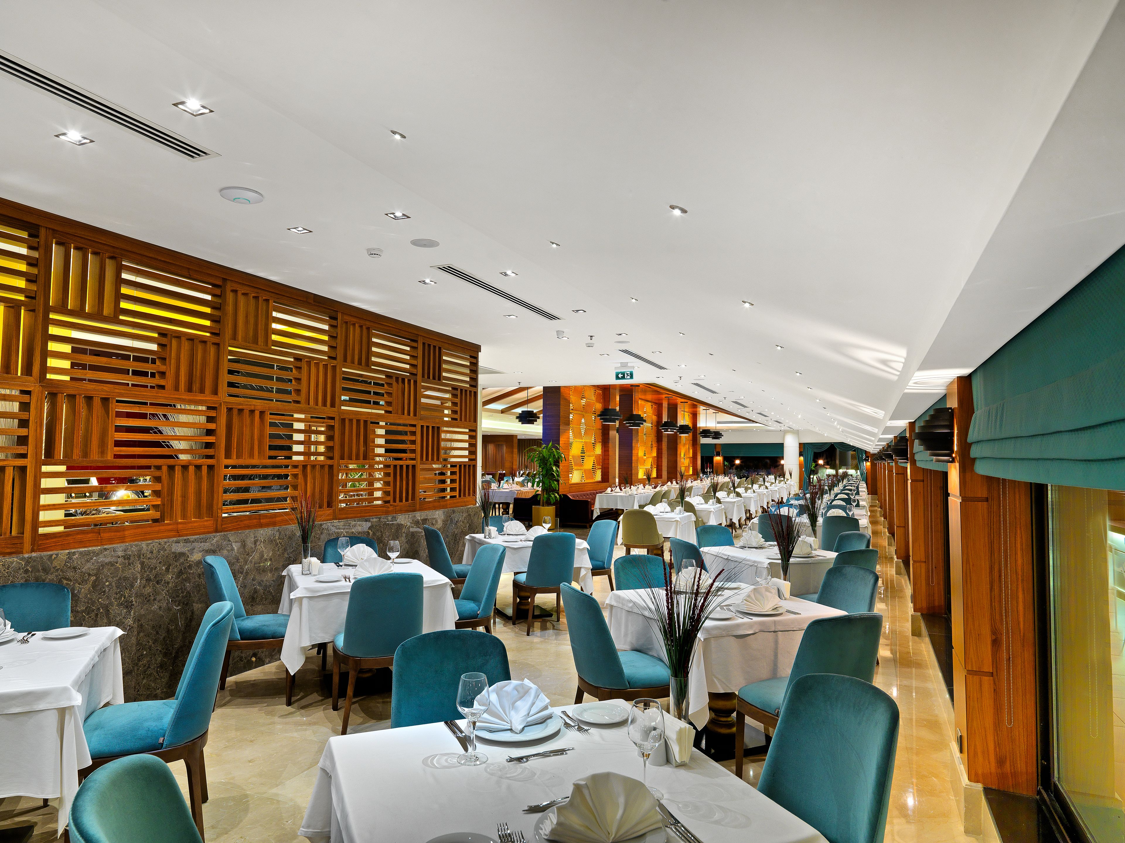 Un restaurant doté de nombreuses tables et chaises, d’un lambris en bois sur un des murs et d’un plafond pourvu d’un éclairage encastré.