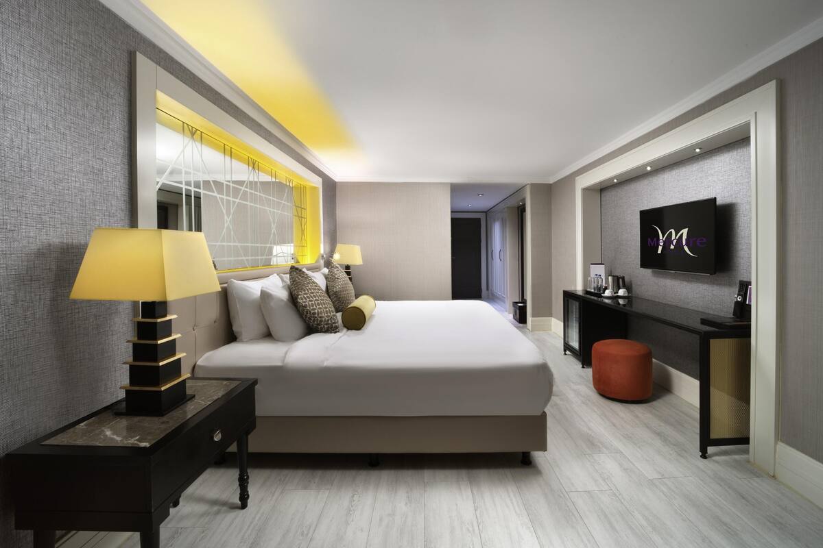 A modern hotel room with a large bed, bedside lamps, a TV, and a small side table.