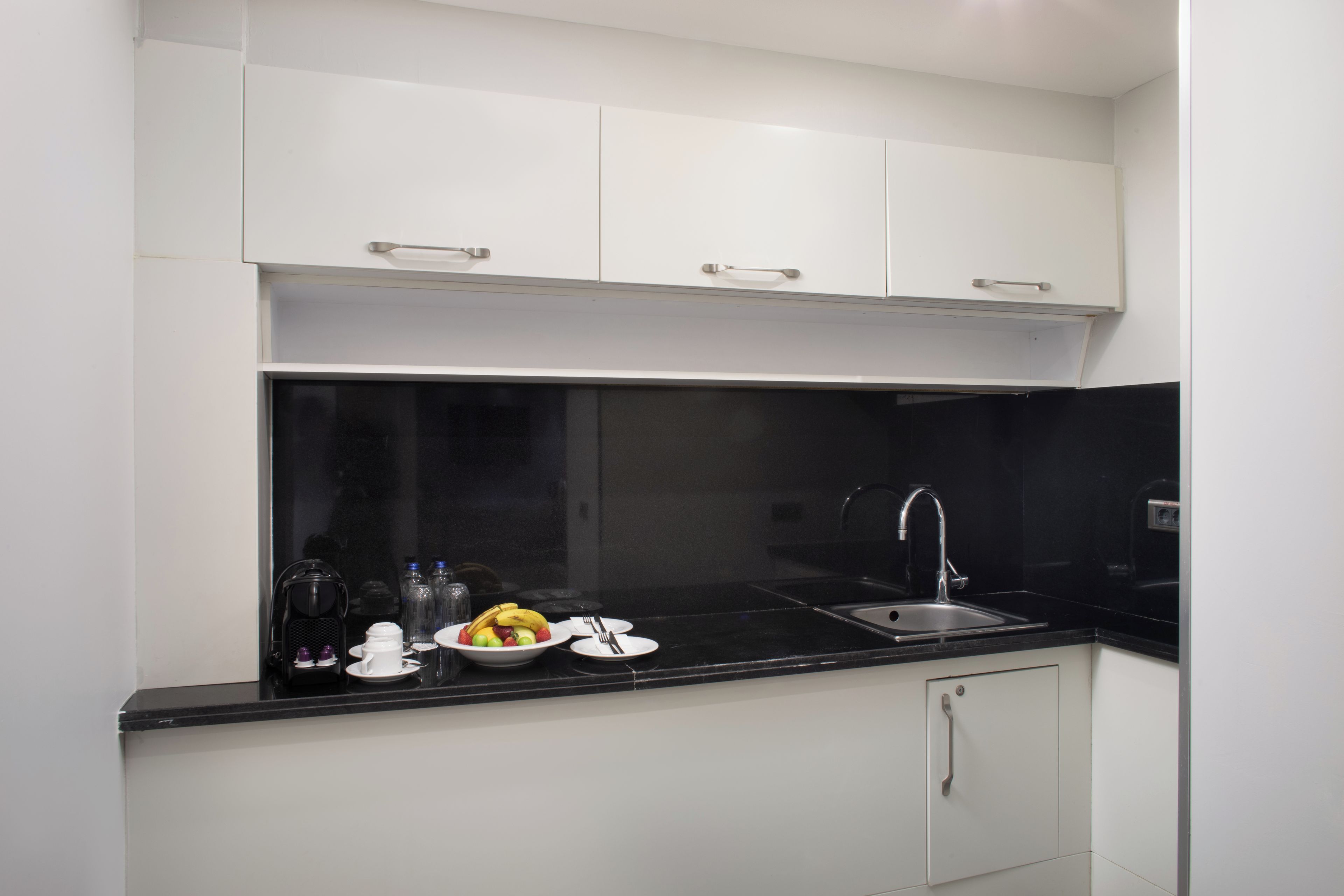 A modern kitchen with white cabinets, a black countertop, and a stainless steel sink.