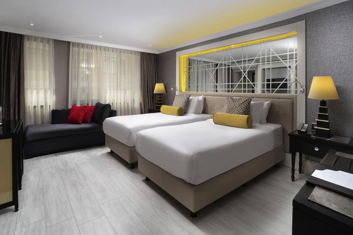 A modern hotel room with two beds, a sofa, and a desk.