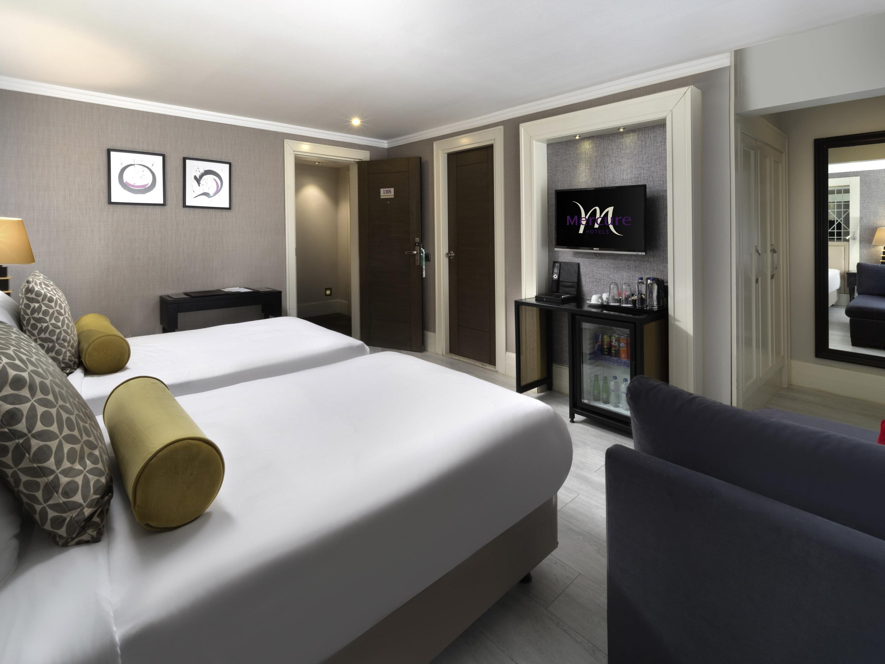 A hotel room with a large bed, a TV, a minibar, and a seating area.