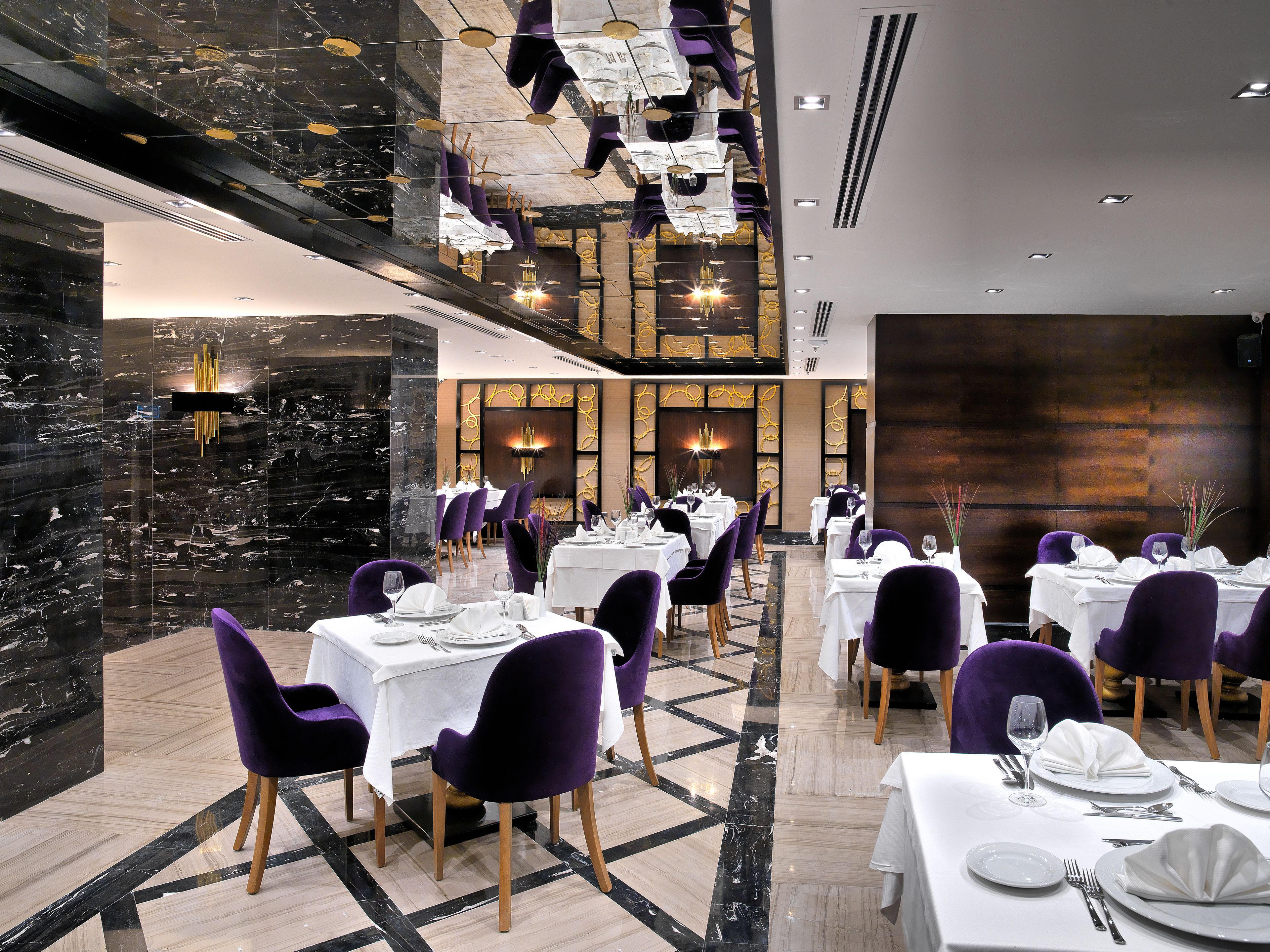 A modern dining area with marble floors, purple chairs, and white tables set for a meal.
