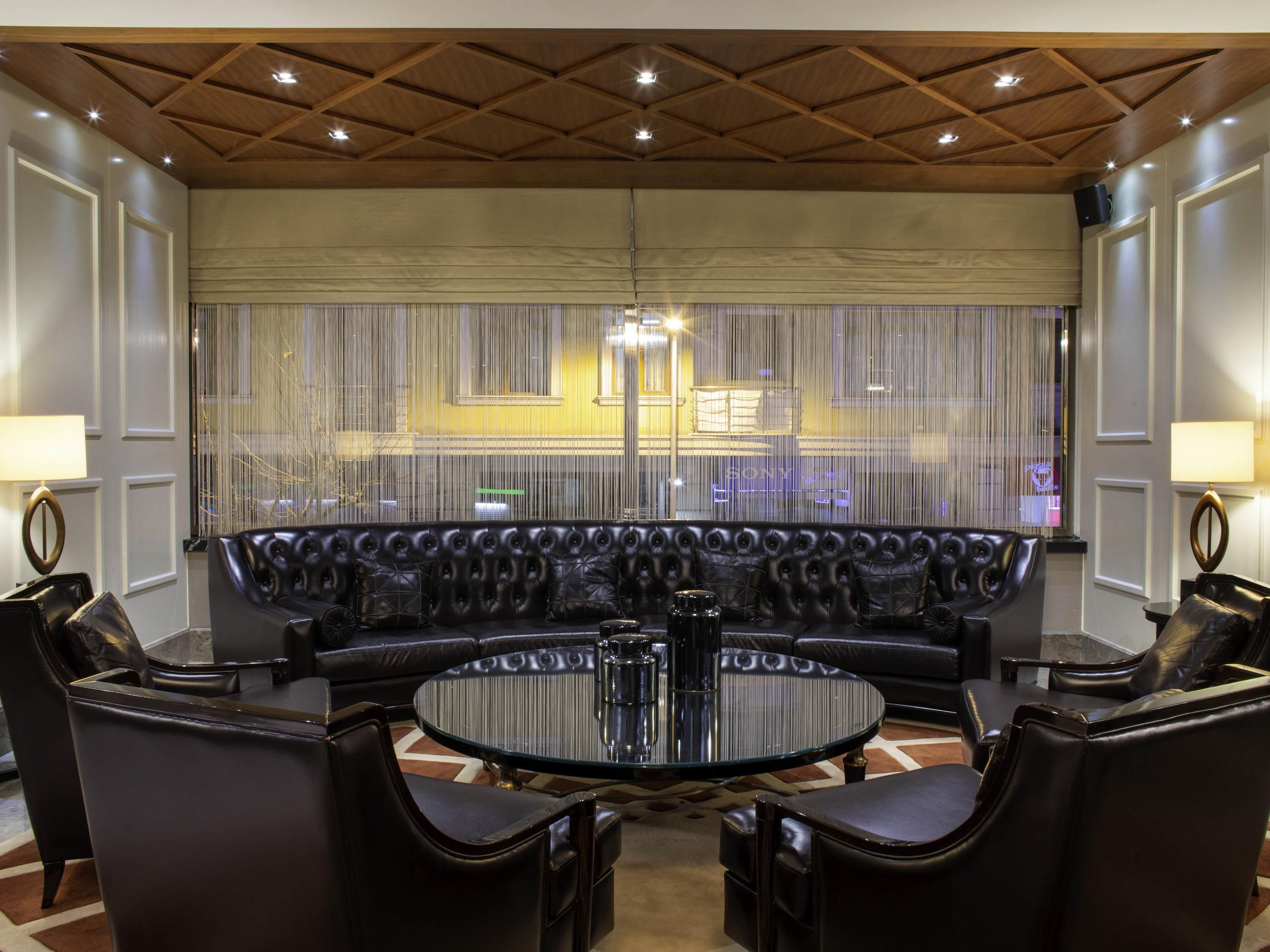Un salon moderne avec un canapé en cuir, une table basse en verre et une vue dégagée sur l’extérieur grâce à une grande fenêtre.