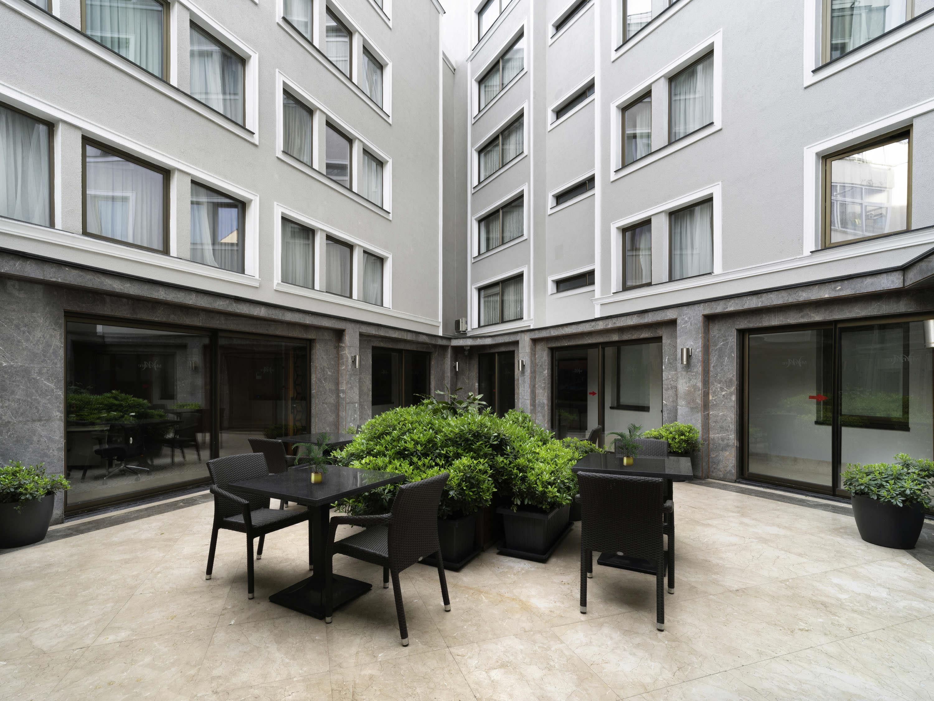 Un pati modern amb una zona de menjador, plantes en testos i un edifici amb nombroses finestres.