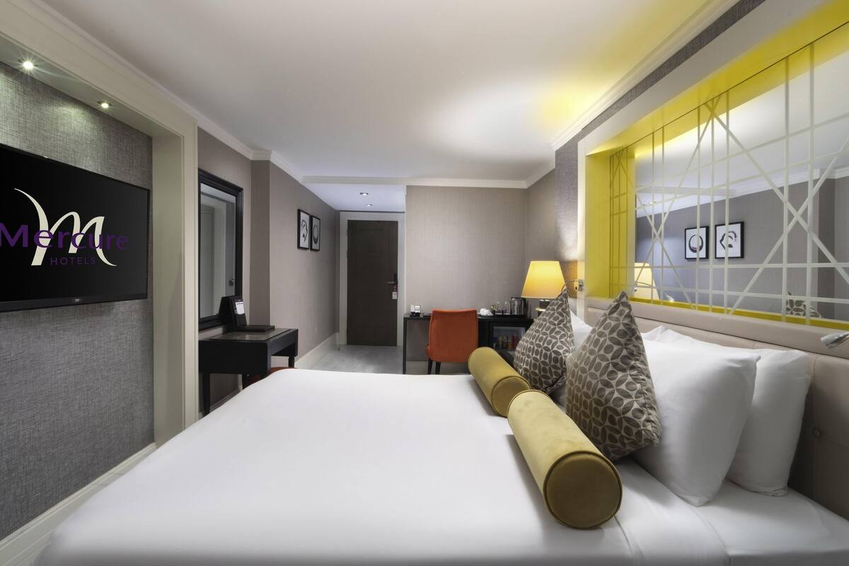A hotel room with a bed, a desk, a chair, a TV, and a lamp.