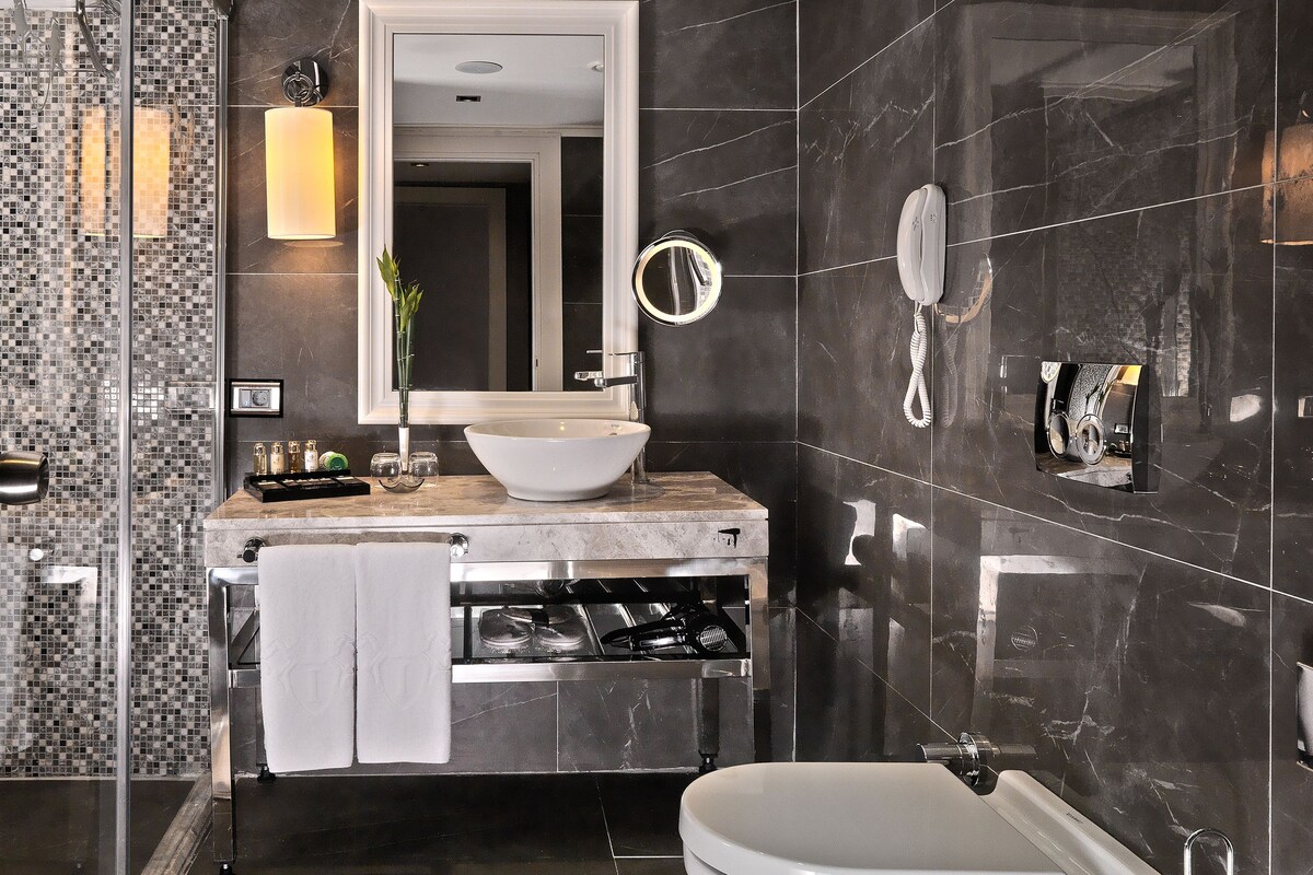 A modern bathroom with a glass-enclosed shower, a large mirror, a sink with a vessel basin, and a toilet.