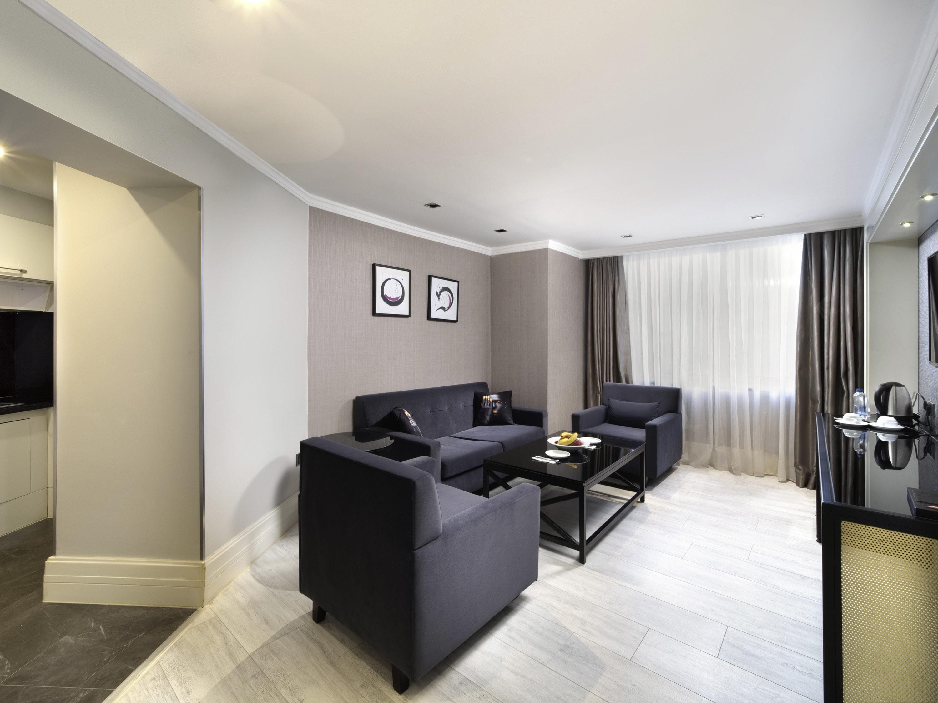 A modern living room with a sofa, armchair, coffee table, and artwork on the wall.