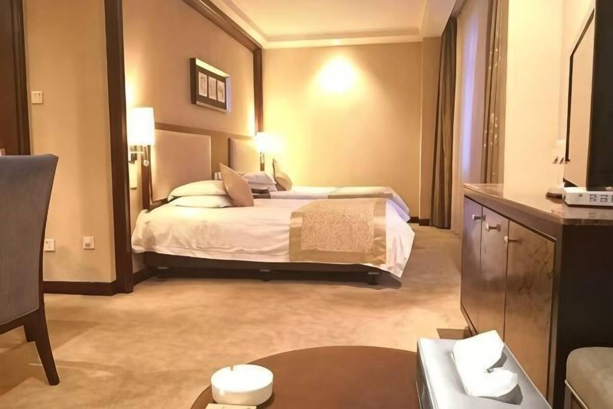 A hotel room with two beds, a desk, a chair, a small table, and a cabinet.