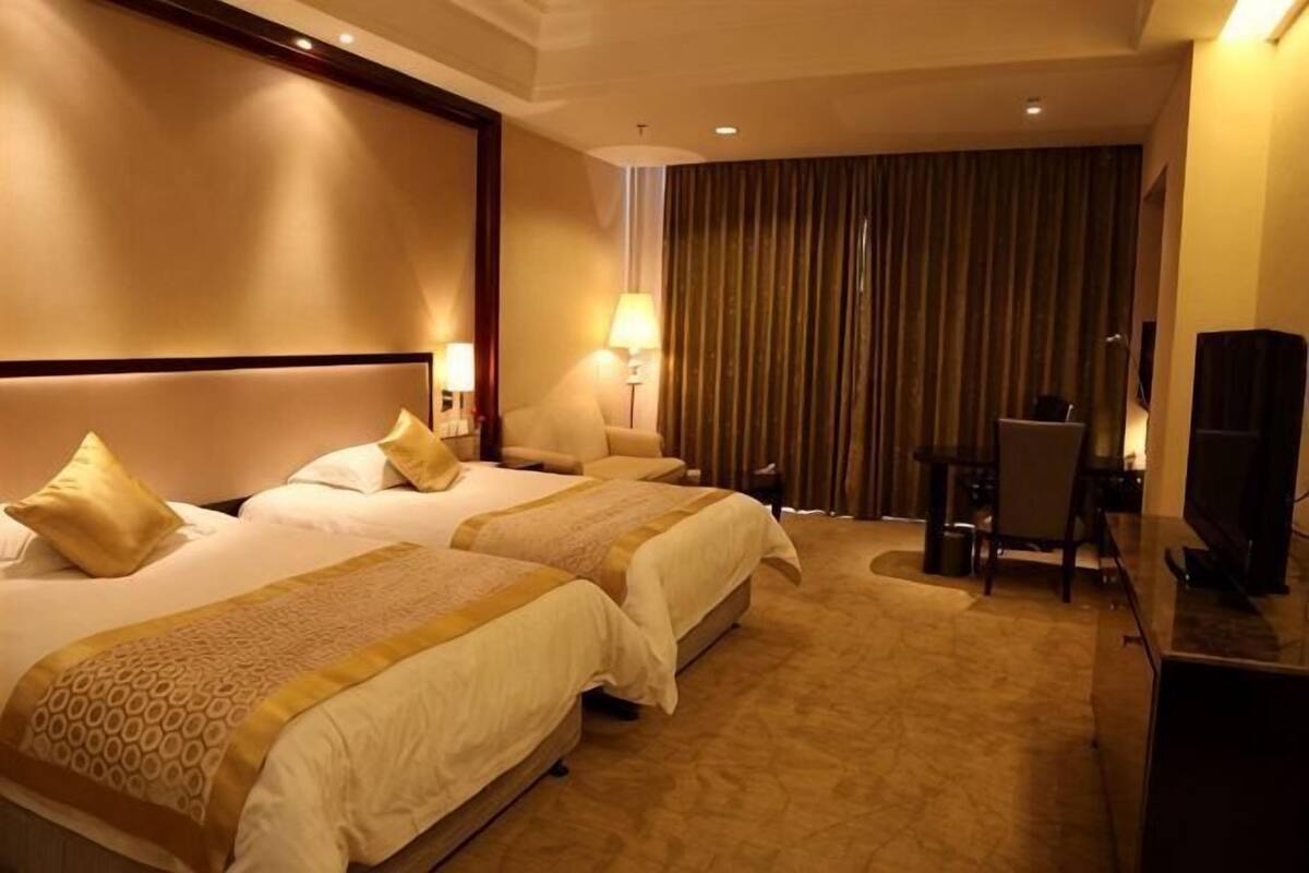 A hotel room with two beds, a desk, a chair, a TV, and a curtain.