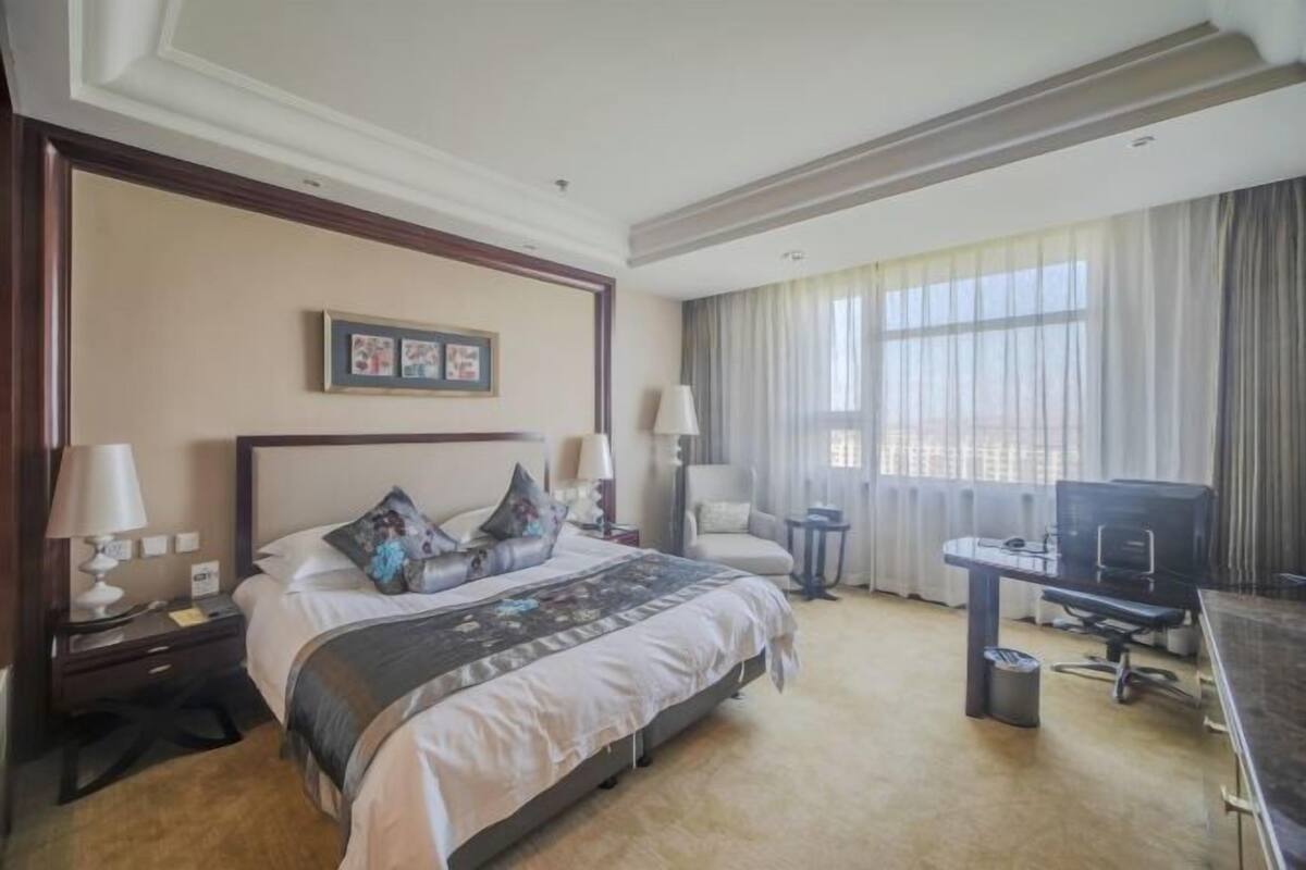 A hotel room with a large bed, a desk with a computer, a TV, and a chair.