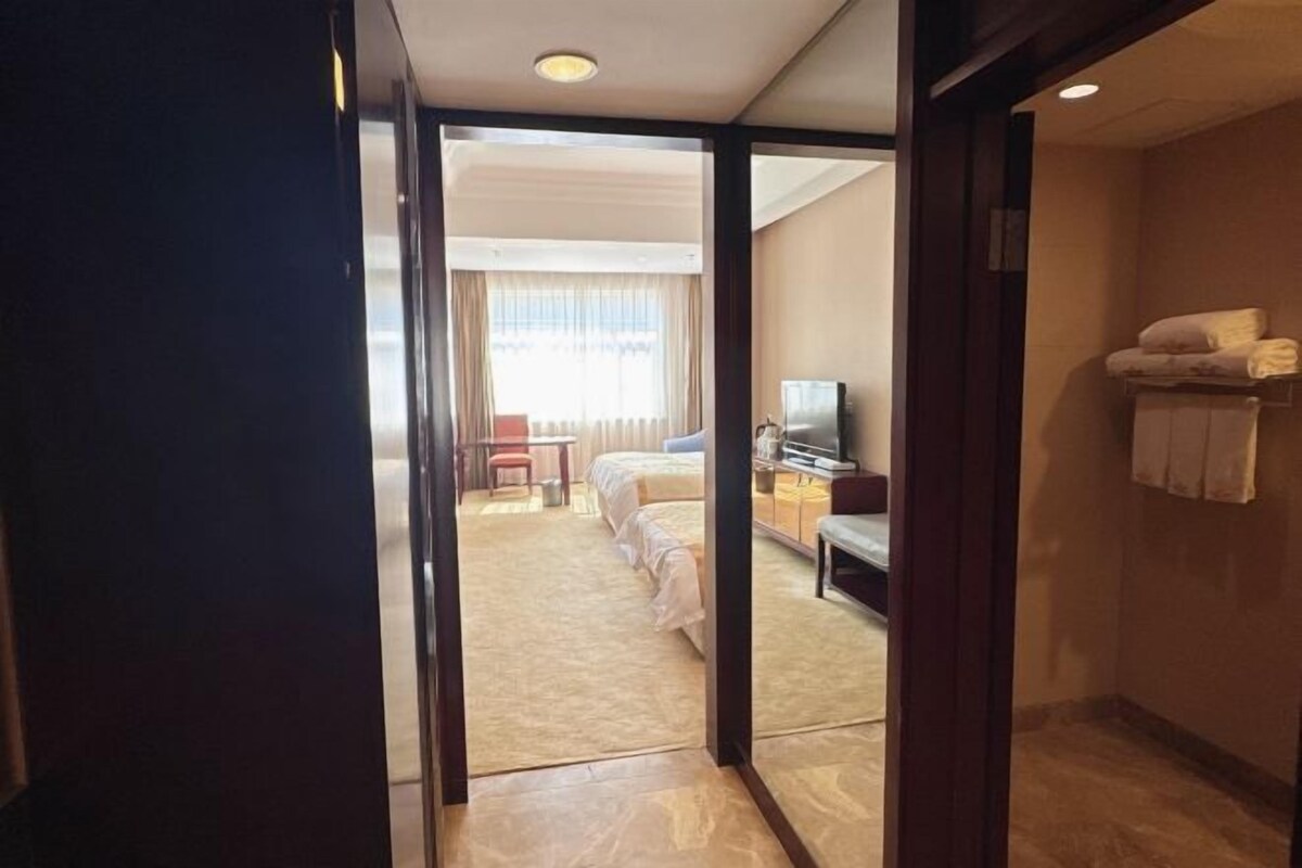 A hotel room with a bed, a desk, a chair, a television, and a bathroom with a towel rack.