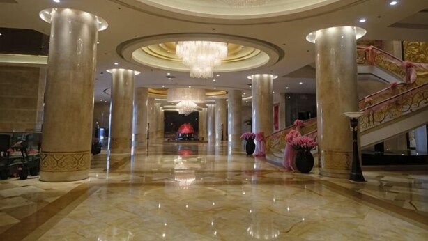 A spacious lobby with high ceilings, large chandeliers, and a grand staircase.