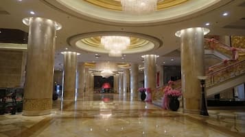 A spacious lobby with a grand staircase, large columns, and a chandelier.