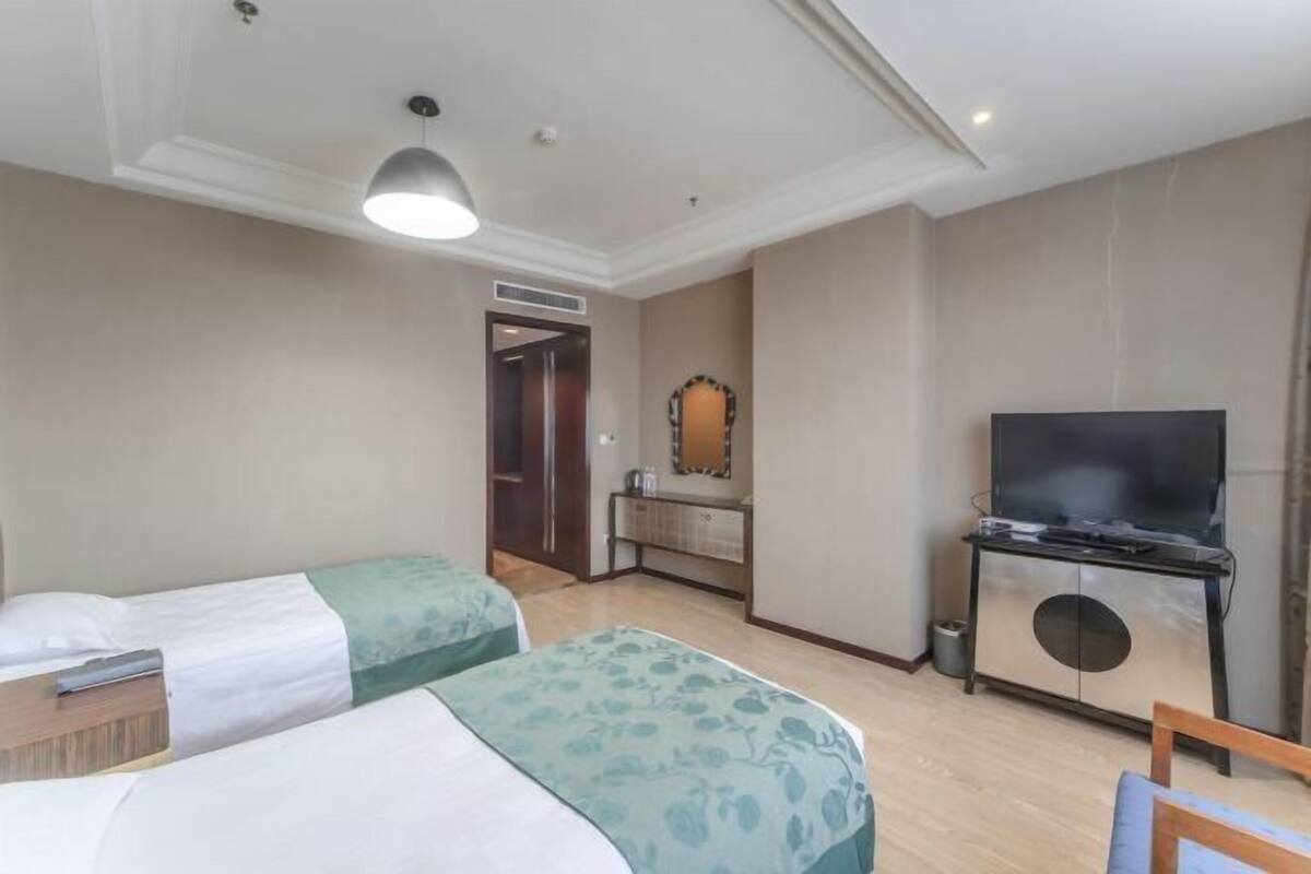 A hotel room with two beds, a TV on a cabinet, a mirror, and a door leading to another room.
