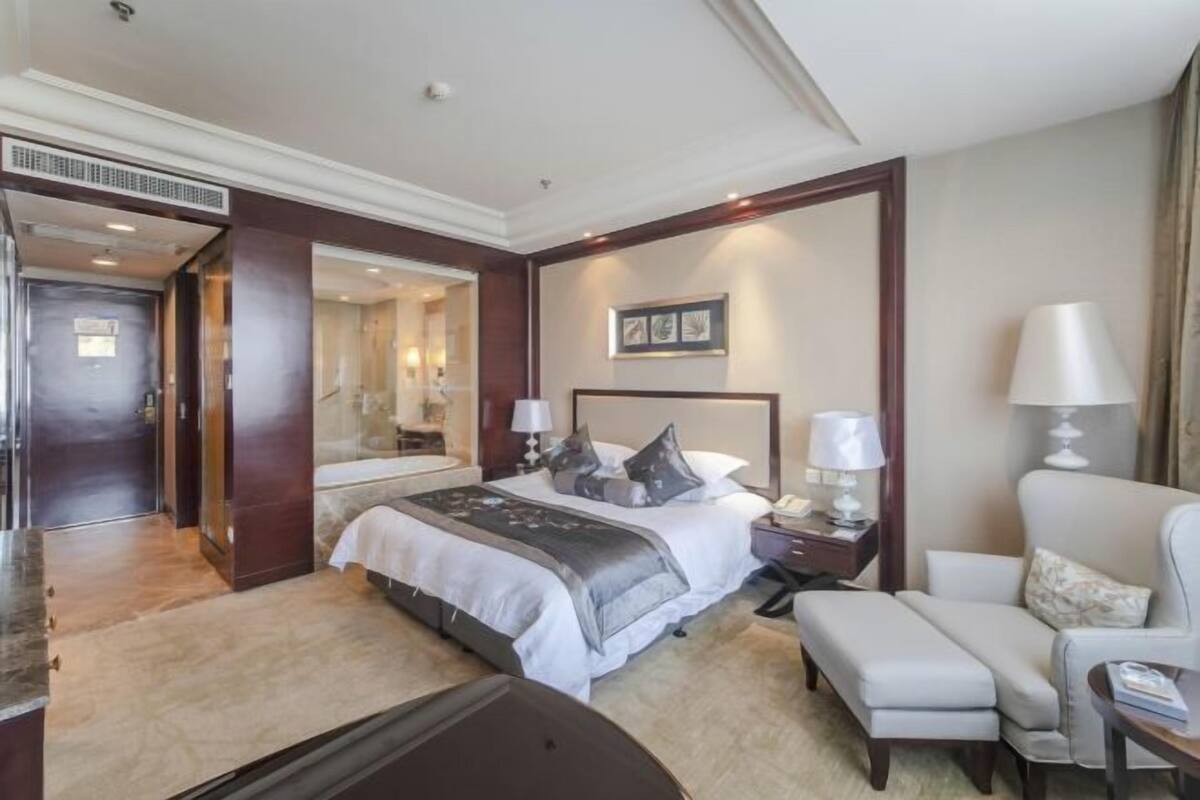 A hotel room with a bed, bedside tables, a chair, a desk, and a mirror.