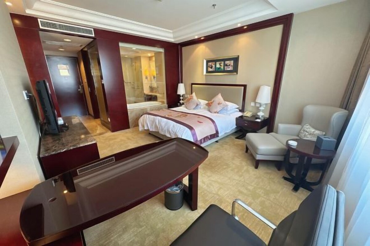 A hotel room with a bed, bedside table, lamp, chair, and a desk with a chair.