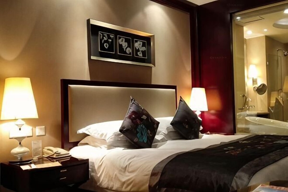 Una habitación de hotel con una cama, lámparas de noche, una mesita de noche, un espejo y un cuadro en la pared.
