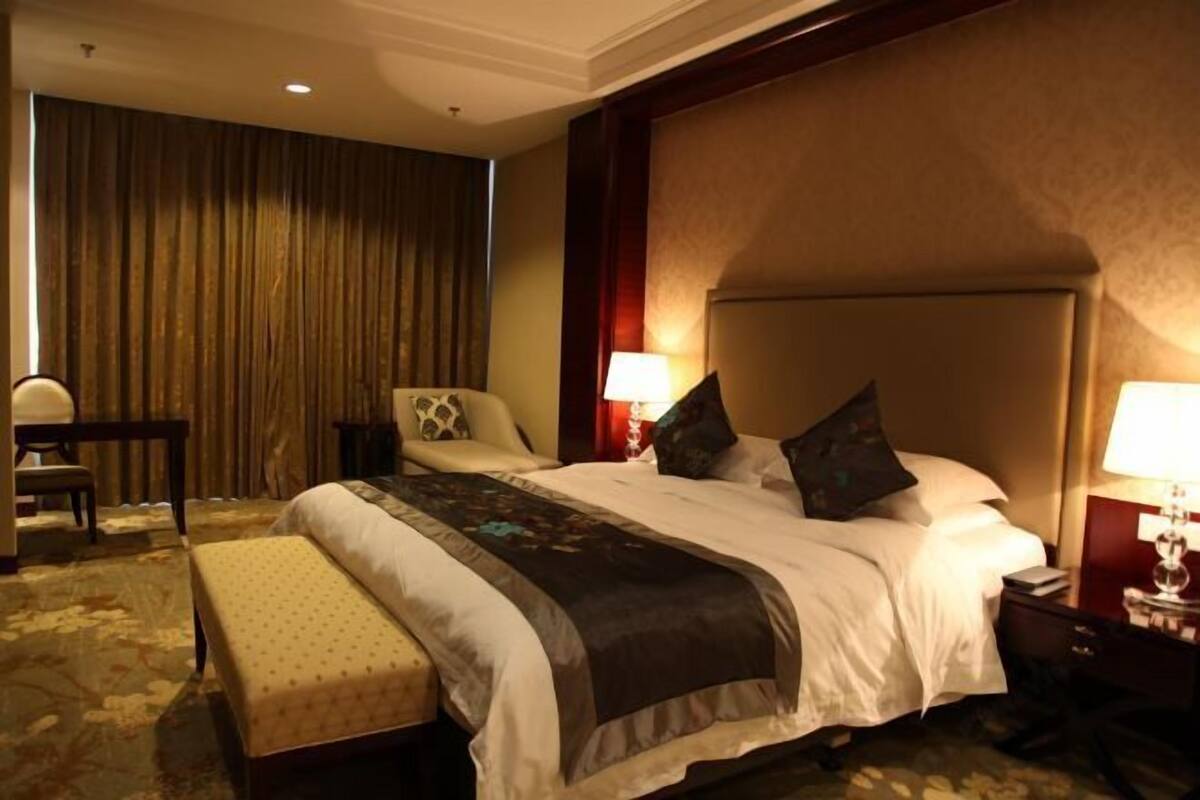 A hotel room with a large bed, a bedside table, a chair, a desk, and a curtain.