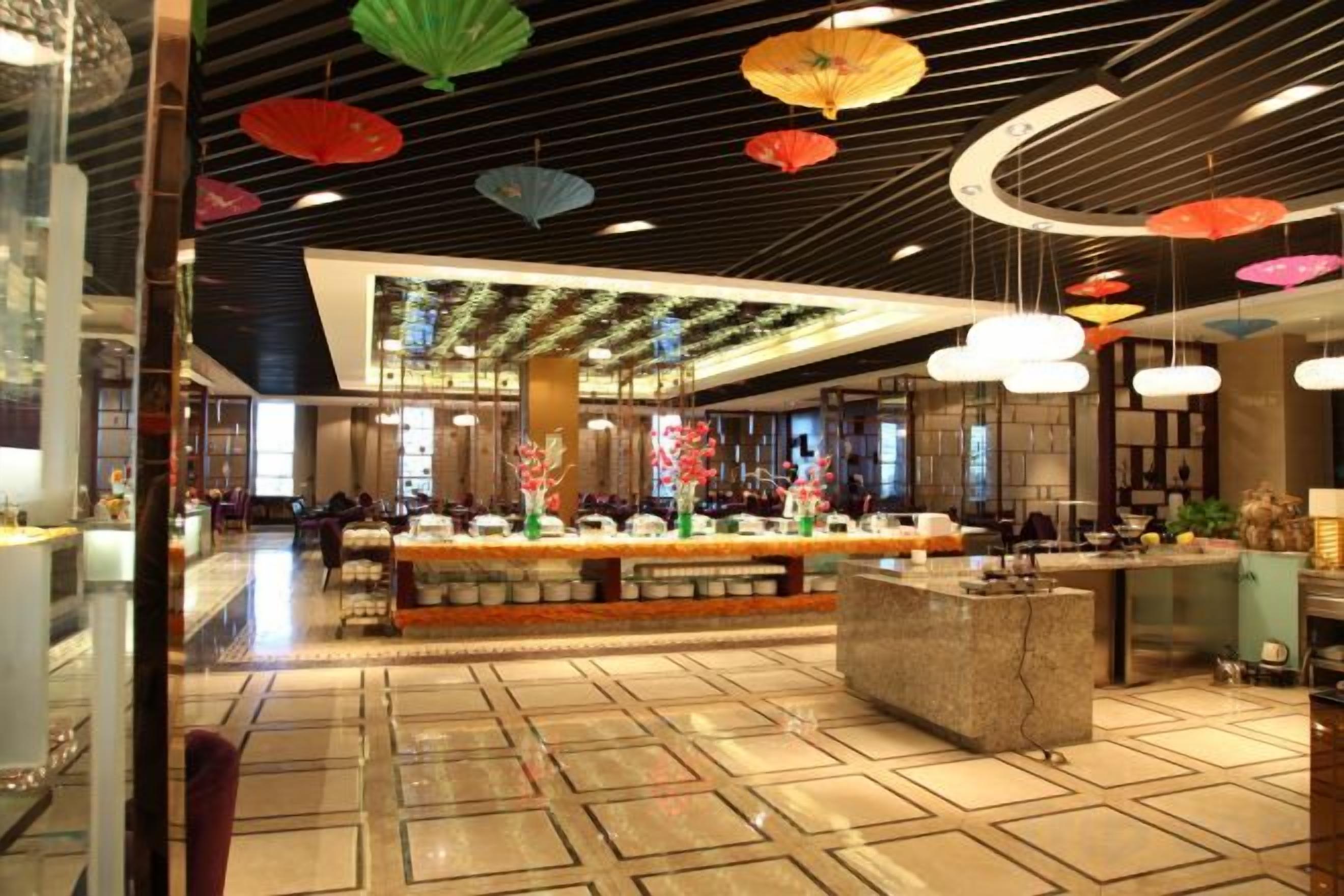 A hotel lobby with a central reception desk, a patterned floor, and hanging umbrellas.