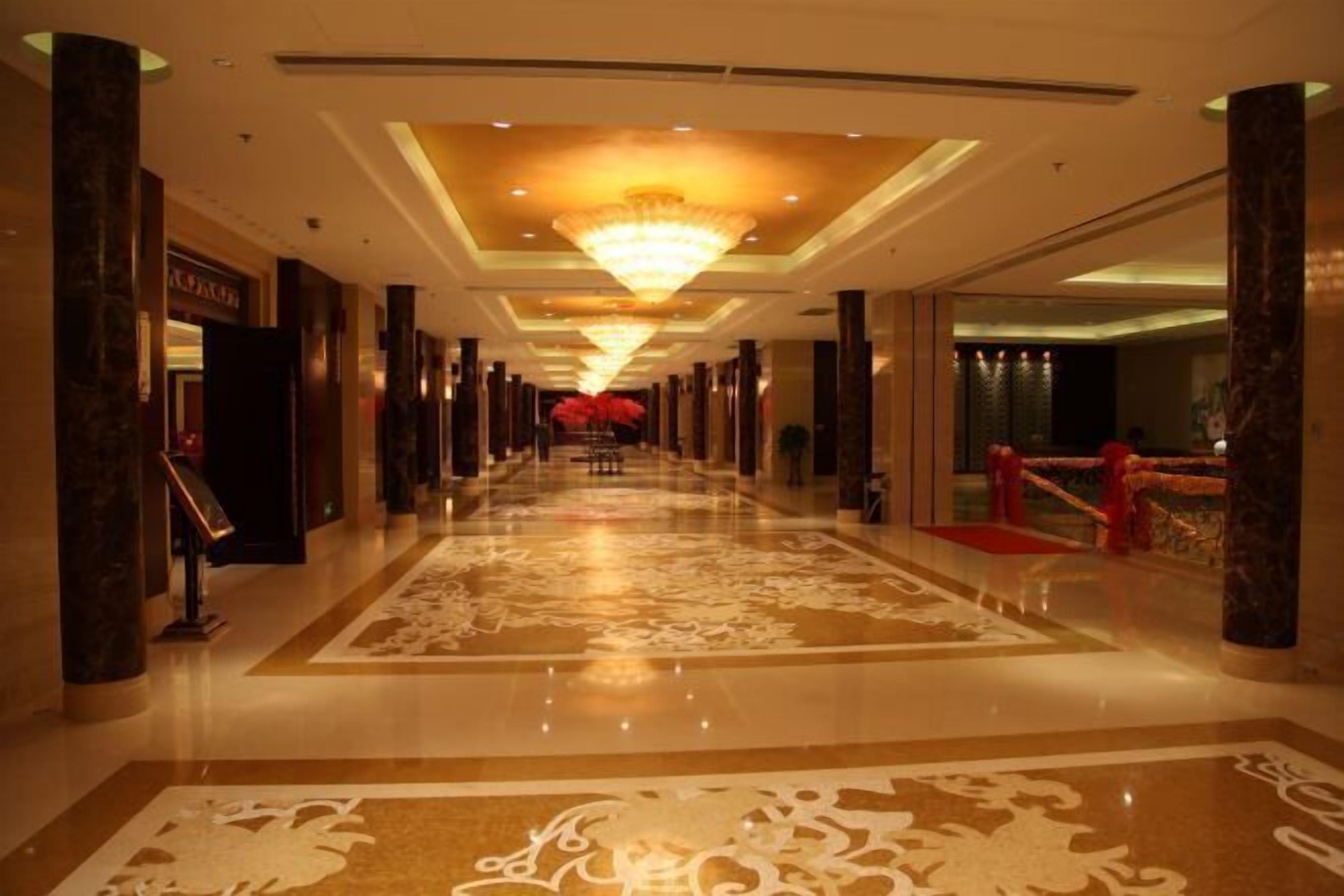 A hotel corridor with a central chandelier, marble columns, and a patterned carpet.