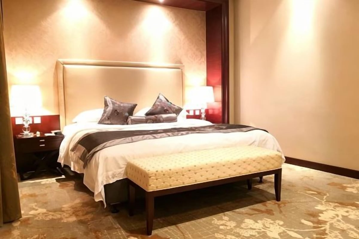 Habitación de hotel con cama, lámparas de noche, un banco y piso alfombrado.