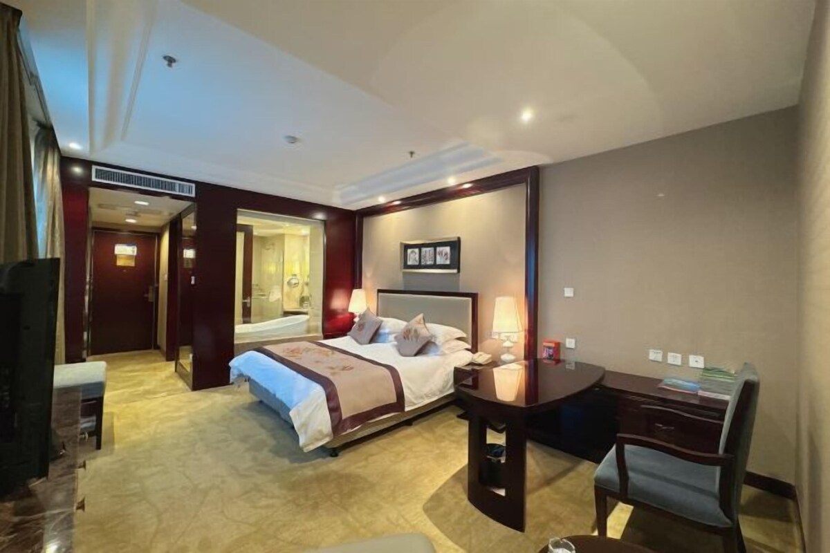 A hotel room with a large bed, a desk, and a chair. There is a television and a mirror.
