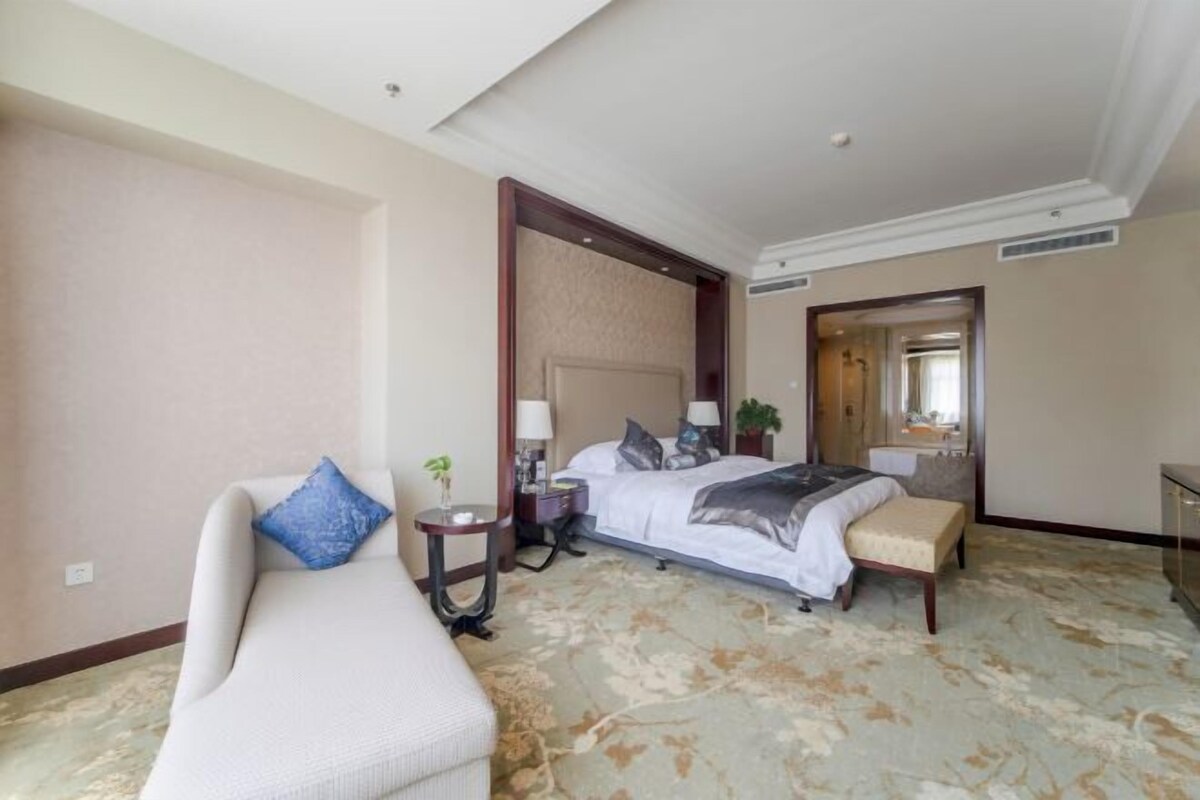 A hotel room with a bed, a sofa, a bedside table, a lamp, and a mirror.