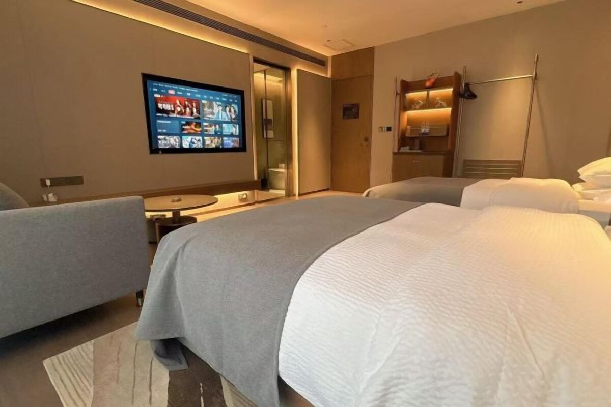 A hotel room with two beds, a TV mounted on the wall, a desk, and a mirror.