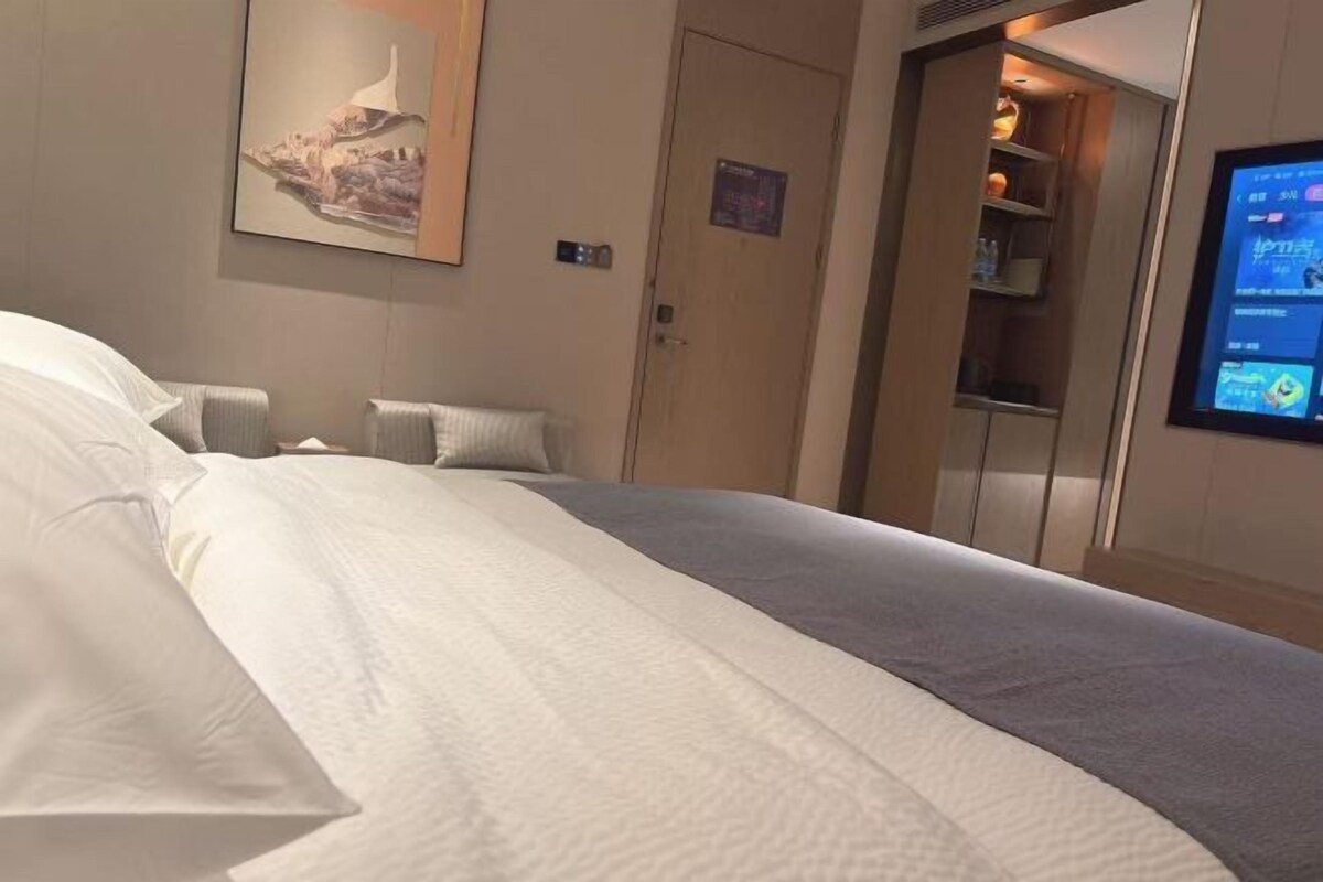 A hotel room with a bed, a wall-mounted TV, and a door leading to a bathroom.