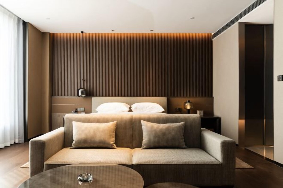 A modern hotel room with a sofa bed, a bedside table, and a lamp.