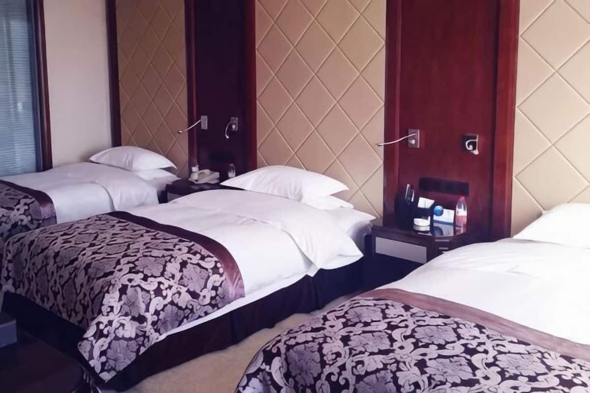 A hotel room with two beds, a nightstand, and a wall-mounted panel.