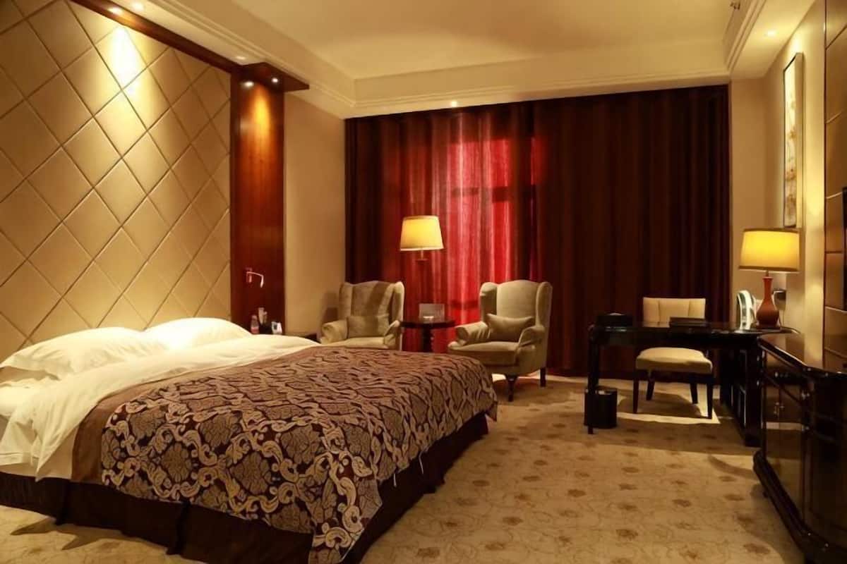 A hotel room with a large bed, two armchairs, a desk, and a red curtain backdrop.