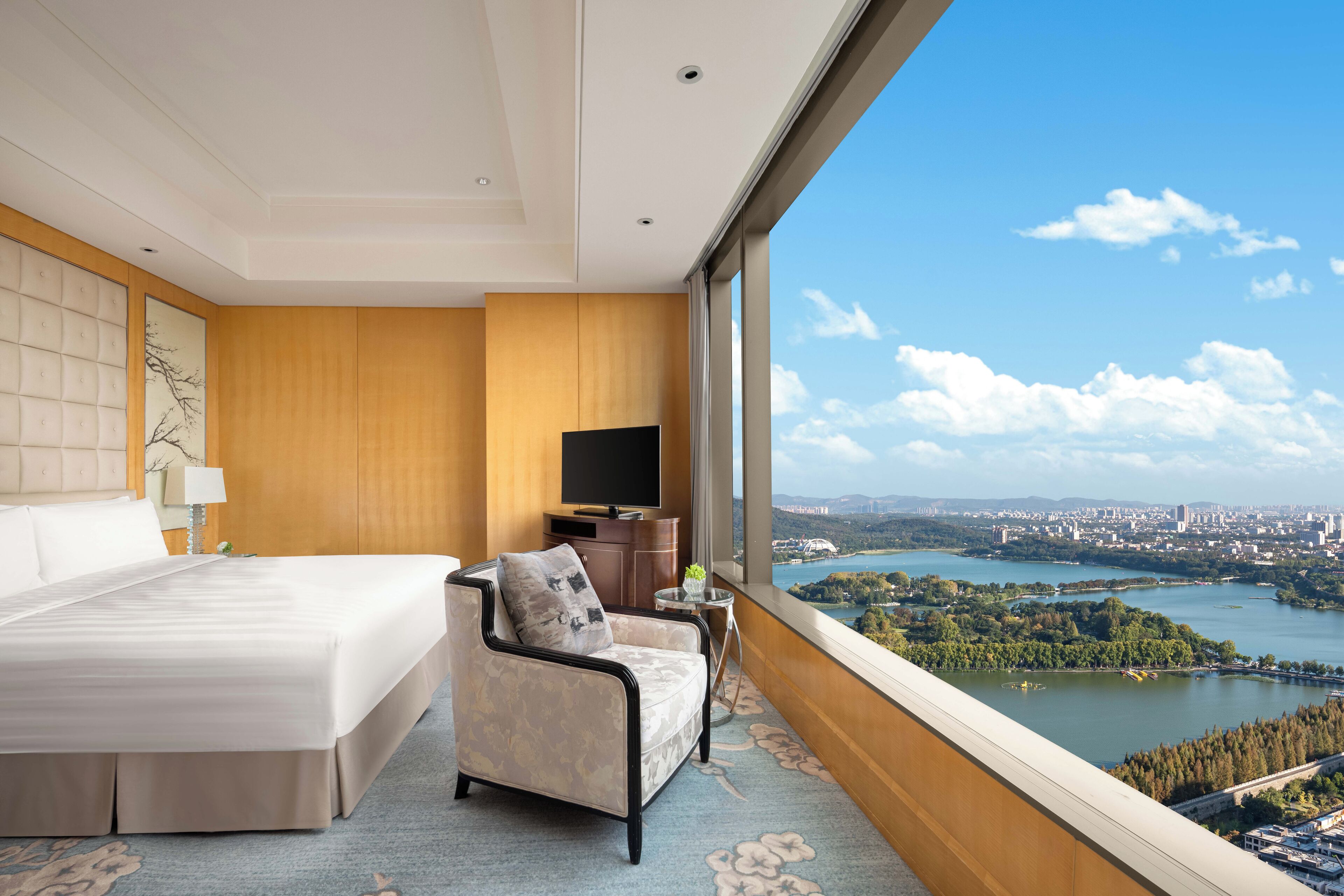Une chambre d’hôtel avec un grand lit, un canapé, une télévision et une vue sur un lac et la ville.
